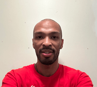 Headshot of Nick Carter wearing a red shirt standing in front of a white wall